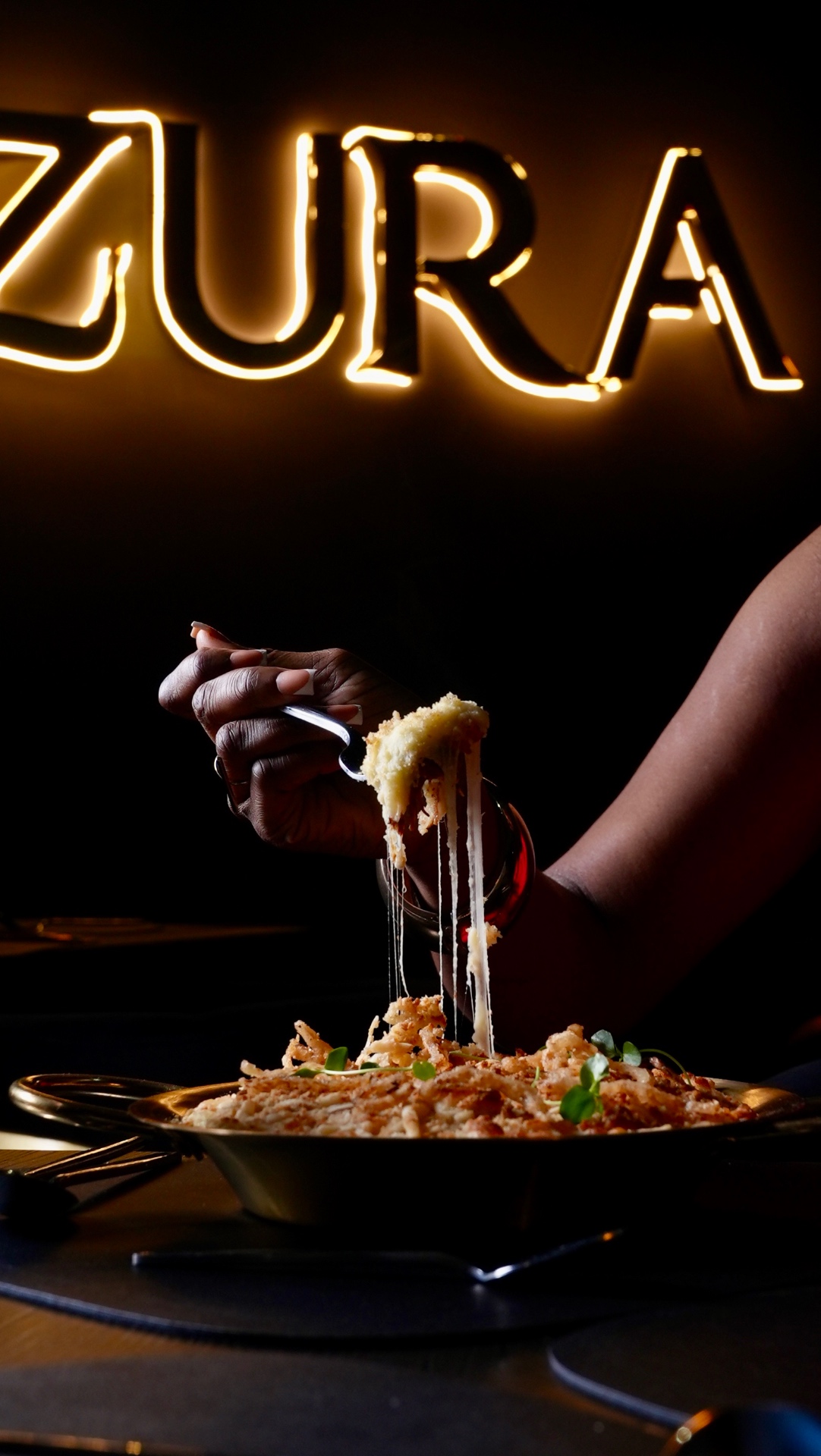 Dining at ZURA, with a freshly served dish beneath the restaurant's glowing sign