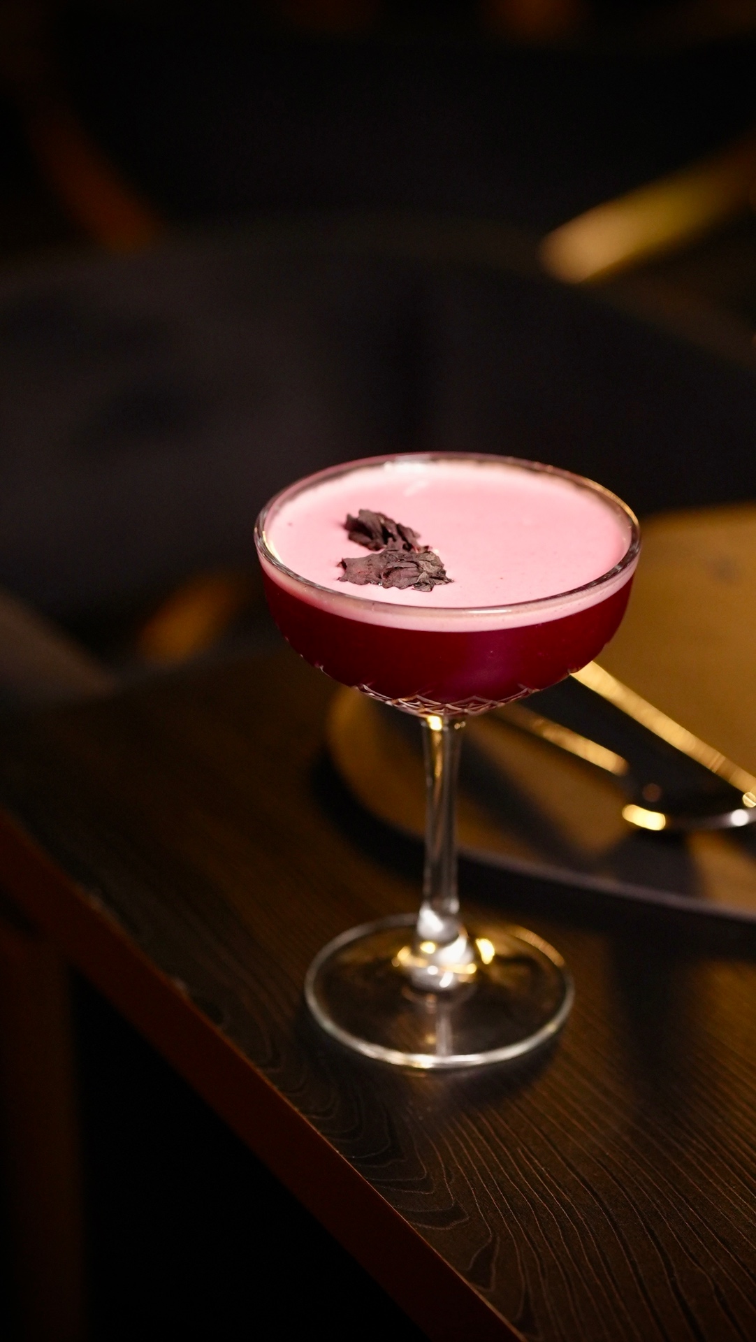 A ruby-red ZURA cocktail with a pink foam top in a coupe glass